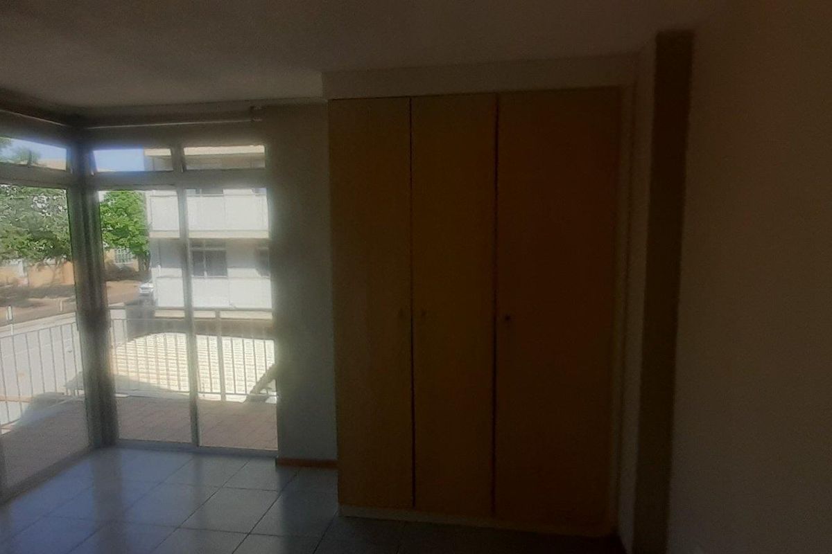 A bedroom featuring built-in wooden cupboards and large sliding glass doors that open onto a balcony, providing natural light and exterior views.