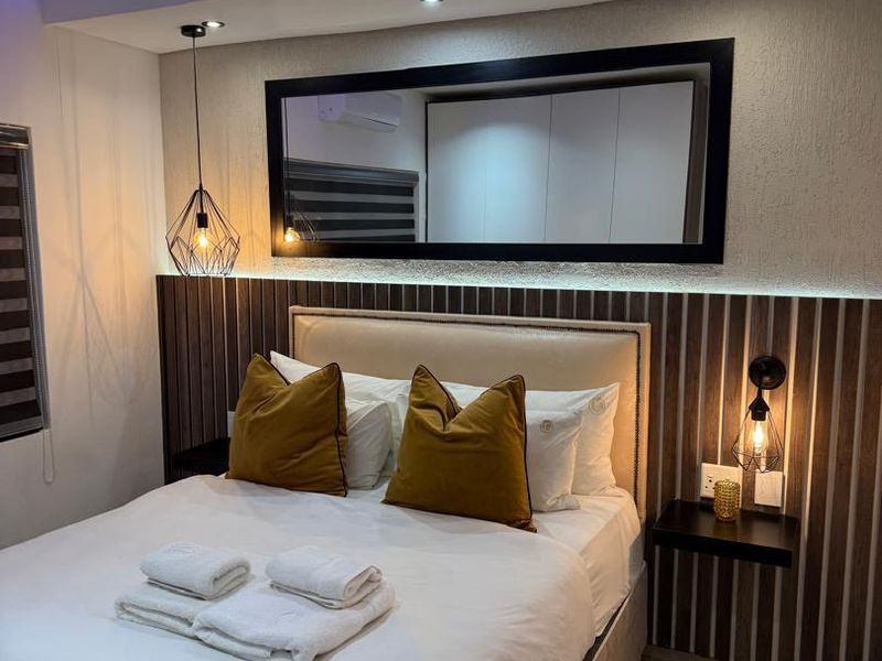 Modern bedroom featuring a custom headboard with integrated lighting, recessed ceiling lights, tiled floors, and built-in wardrobe storage.
