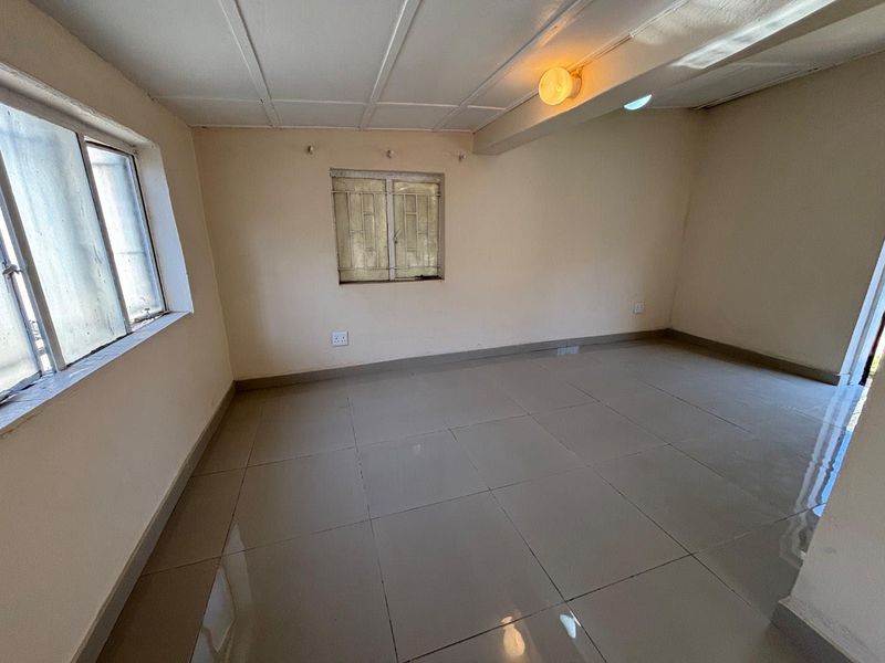 An empty living area featuring tiled flooring, security bars on the windows, and a simple ceiling finish, offering a blank canvas for renovation.