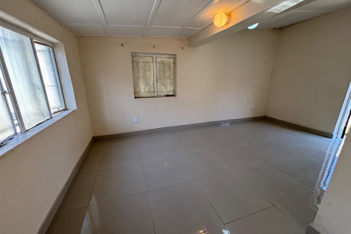 An empty living area featuring tiled flooring, security bars on the windows, and a simple ceiling finish, offering a blank canvas for renovation.