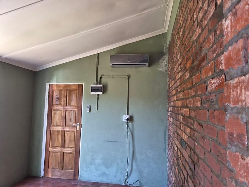 An interior space featuring an exposed brick wall, tiled flooring, and an installed air conditioning unit with visible wall finish wear.