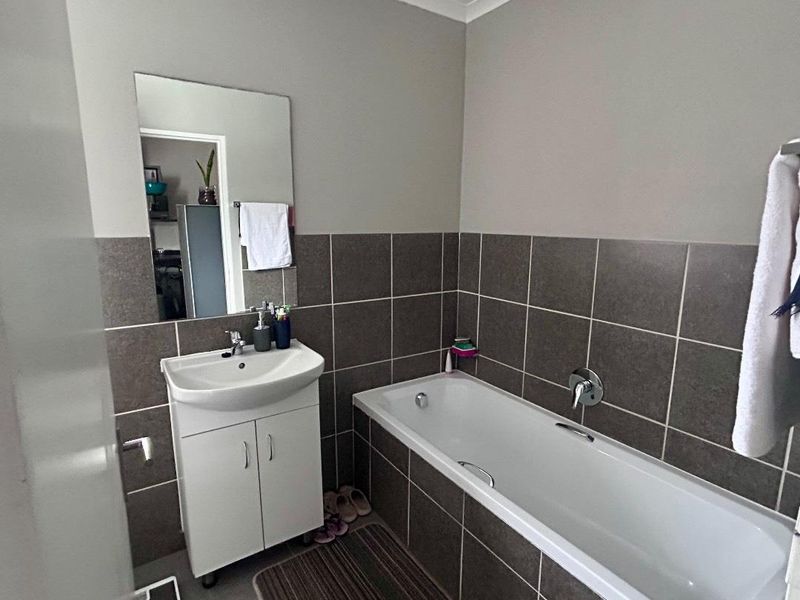 A functional bathroom featuring a white vanity cabinet with a basin, a bathtub with chrome fixtures, and neutral-toned wall tiling.