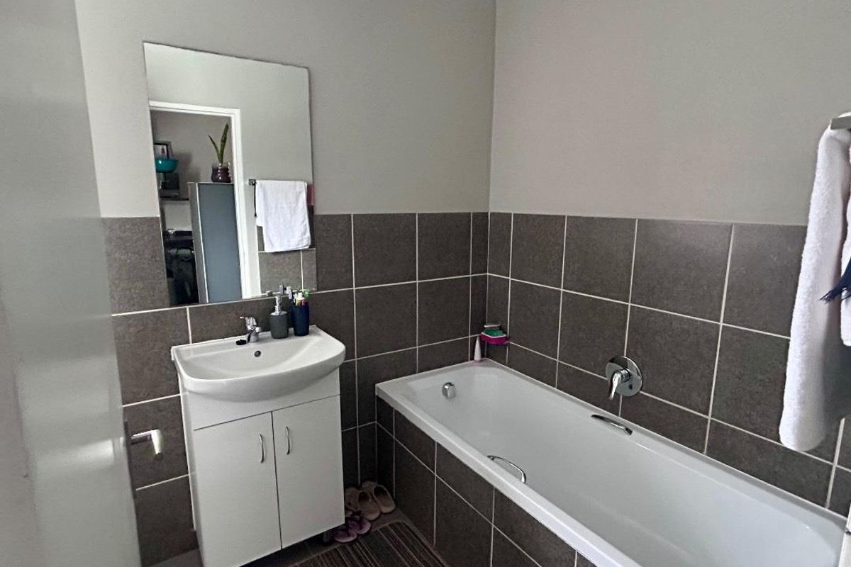 A functional bathroom featuring a white vanity cabinet with a basin, a bathtub with chrome fixtures, and neutral-toned wall tiling.