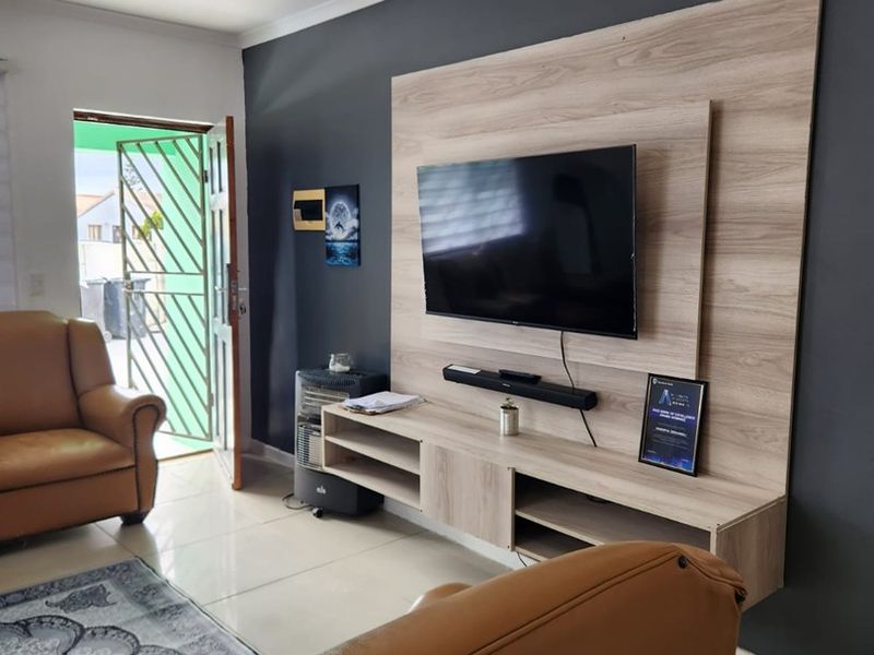 A living room featuring a modern wood-look built-in media unit against a dark accent wall, tiled flooring, and a security gate at the entrance.