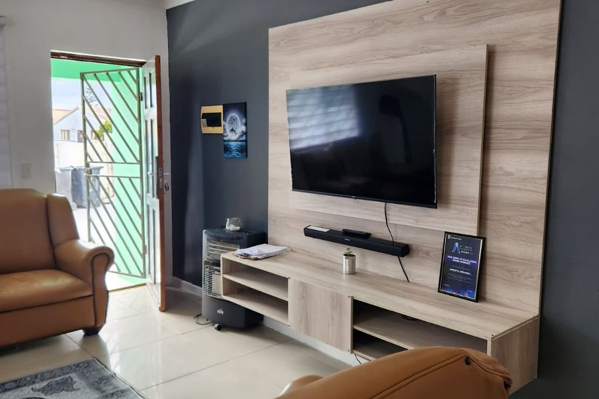 A living room featuring a modern wood-look built-in media unit against a dark accent wall, tiled flooring, and a security gate at the entrance.