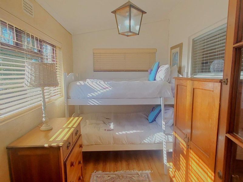A compact bedroom featuring timber flooring, natural light through venetian blinds, and a classic ceiling light fixture.