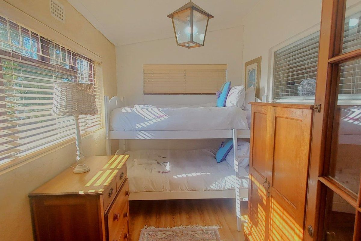 A compact bedroom featuring timber flooring, natural light through venetian blinds, and a classic ceiling light fixture.