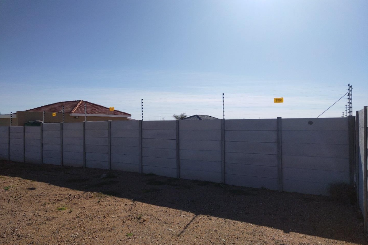 A vacant residential plot featuring a secure precast concrete boundary wall topped with electric fencing.