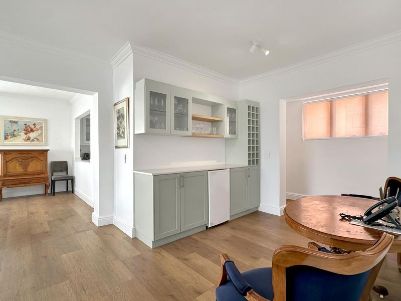 A bright living area featuring custom sage green built-in cabinetry with integrated wine storage, crown molding, and modern laminate flooring.
