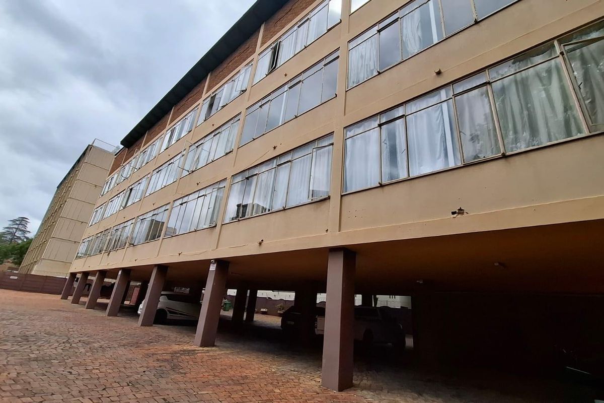 Exterior view of a multi-story apartment building featuring a ground-level covered parking area and large window banks across the residential levels.