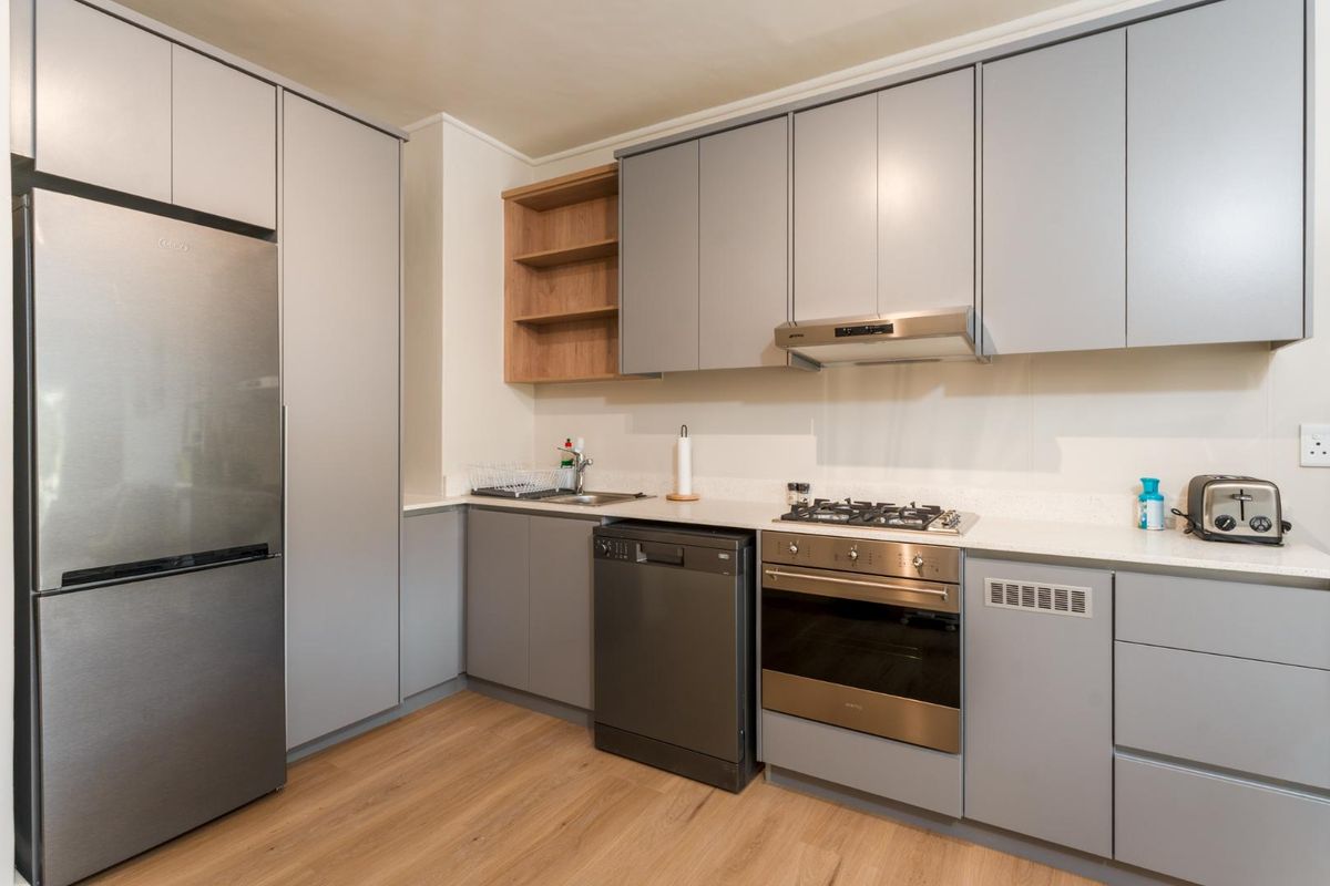 Modern kitchen featuring sleek grey cabinetry, light wood-look flooring, stone countertops, and integrated stainless steel appliances including a gas hob and oven.