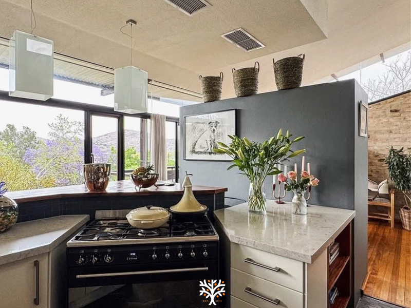 Modern kitchen featuring stone countertops, a gas range, and integrated oven, set against a backdrop of large windows with scenic views.