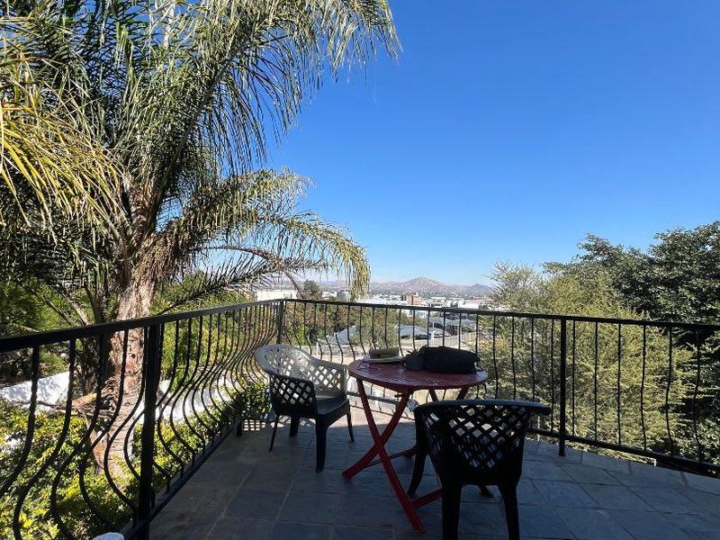 An elevated balcony featuring stone tile flooring and a wrought iron railing, offering expansive views of the surrounding landscape.