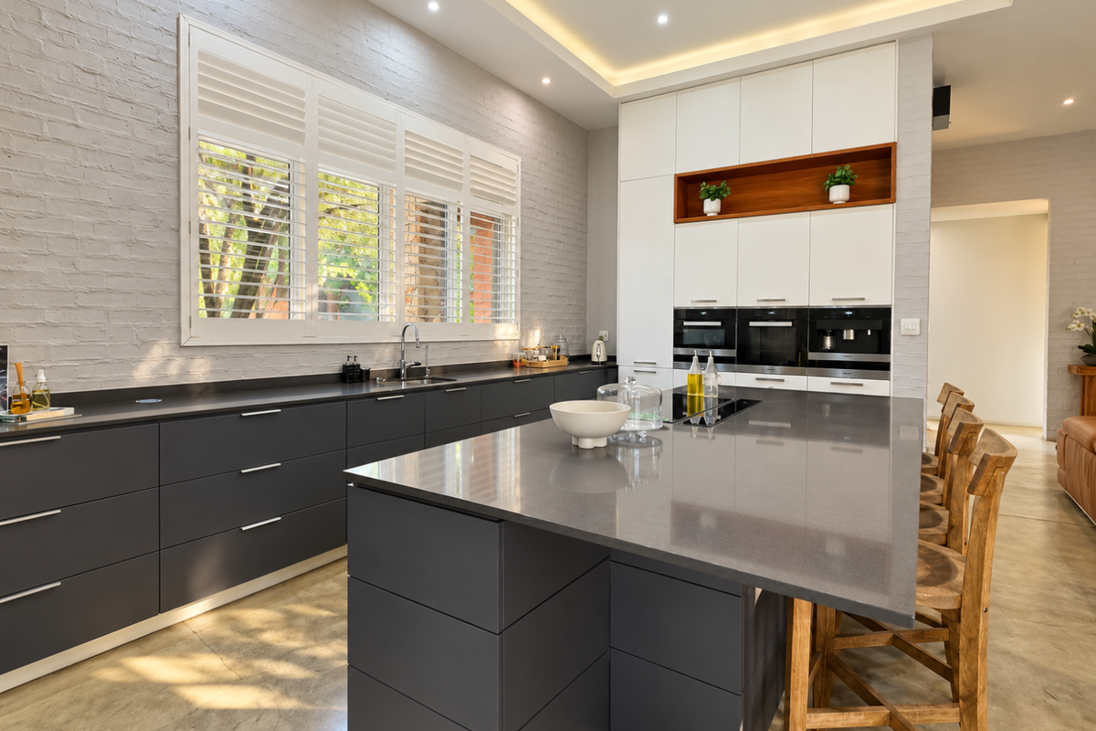 Modern kitchen featuring a large central island, dark cabinetry, quartz countertops, built-in appliances, and stylish exposed brick walls with recessed lighting.