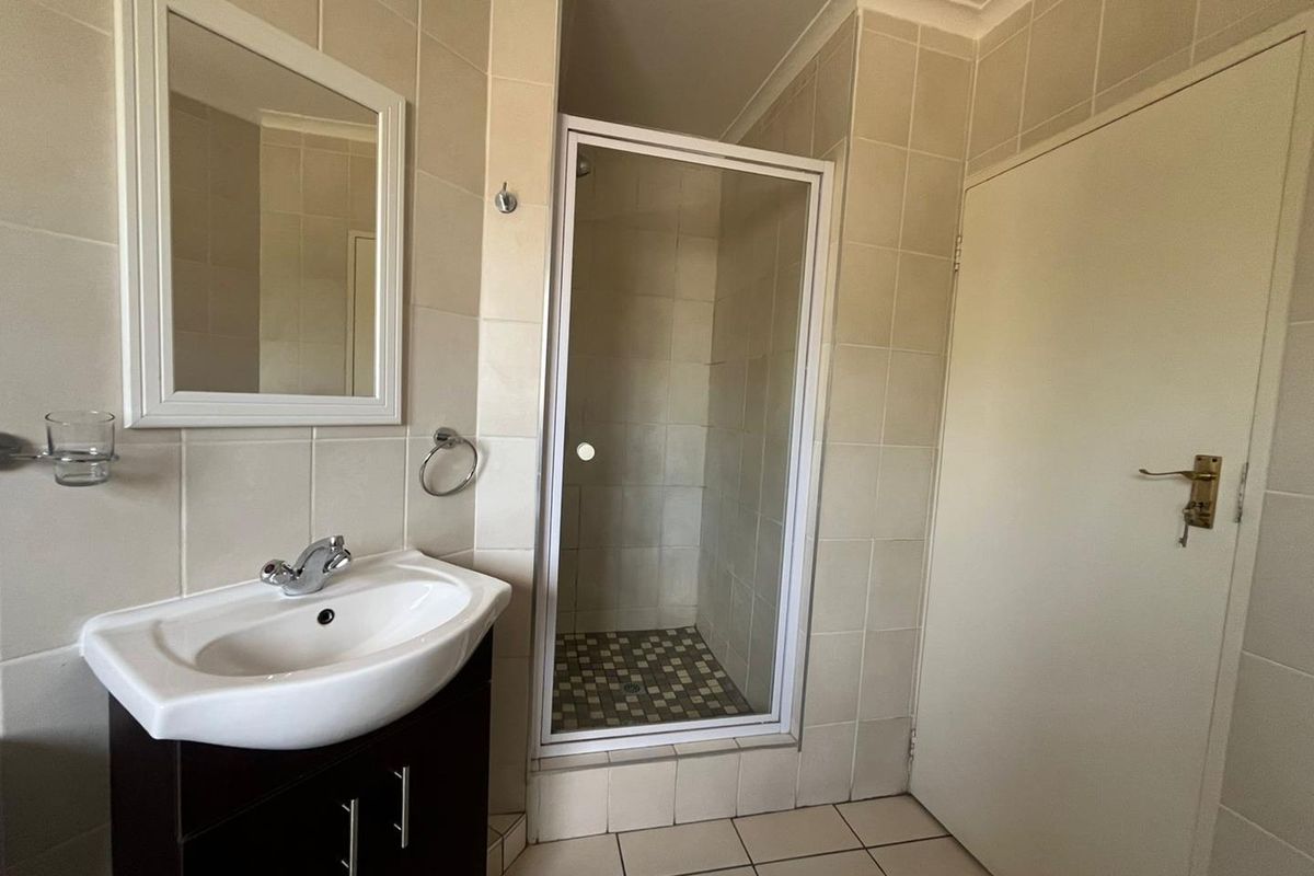 A functional bathroom featuring a tiled shower enclosure, a vanity basin with a mirror, and neutral wall and floor tiling.