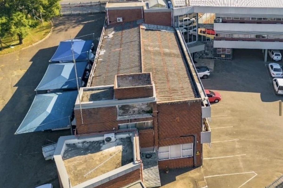 Aerial view of a commercial property featuring a brick building with corrugated metal roofing, adjacent parking area, and shade cloth carports.