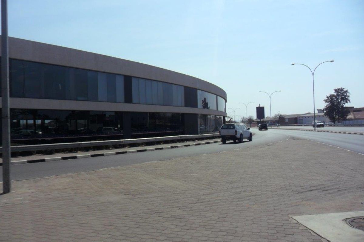 Street-level view of a modern commercial office building featuring extensive glass curtain walling and paved pedestrian access.