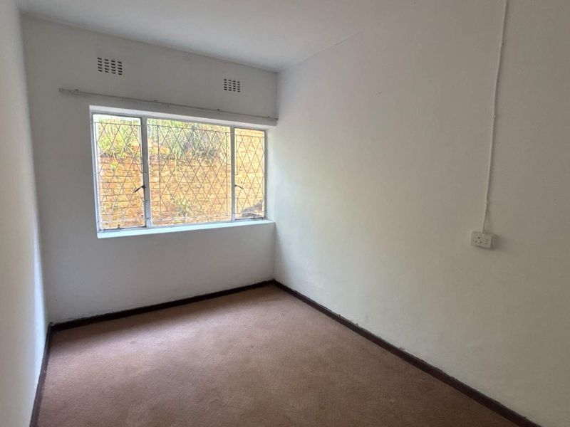 An empty bedroom featuring carpeted flooring, a window with security bars, and visible surface-mounted electrical wiring.