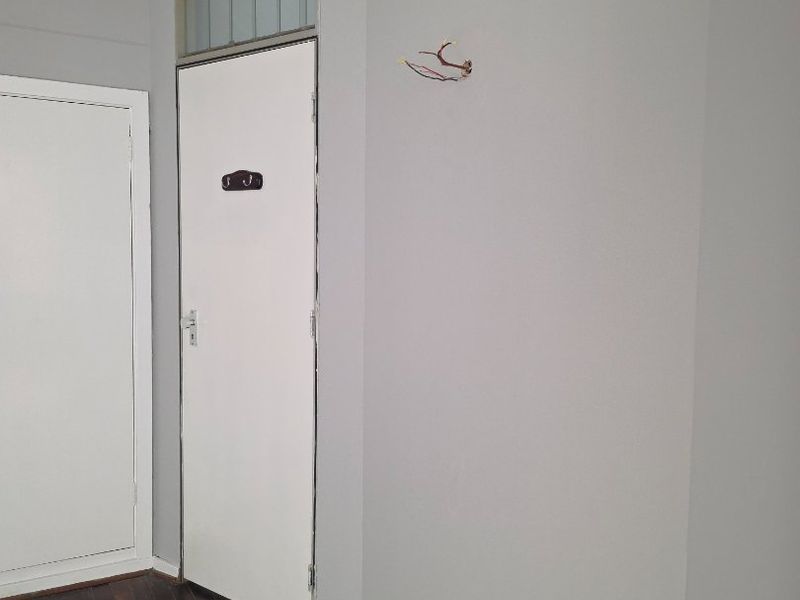 A vacant hallway featuring dark parquet flooring, a white door with a transom window, and exposed electrical wiring on the wall.