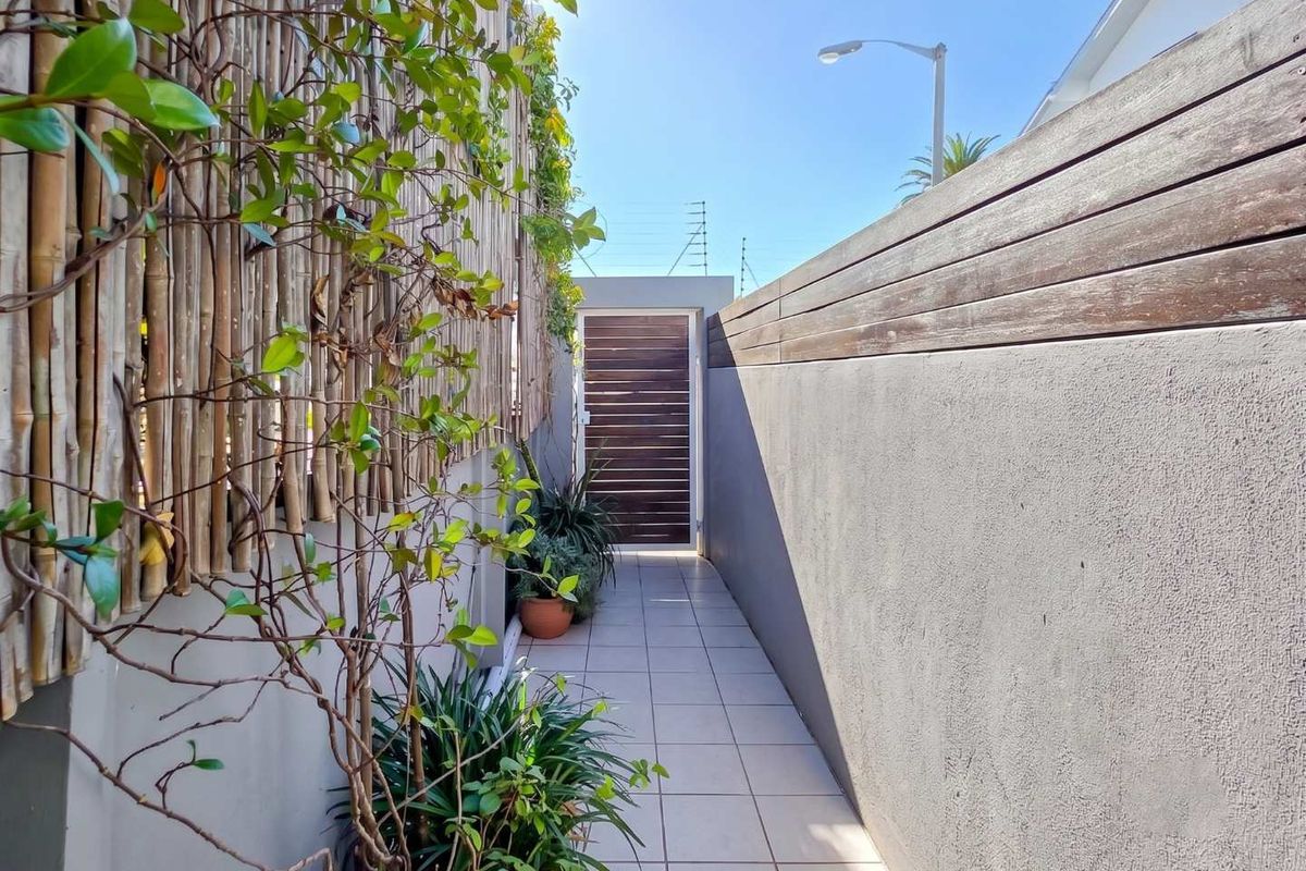 A narrow outdoor walkway featuring tiled flooring, timber slat fencing, and bamboo screening, leading to a secure timber gate.