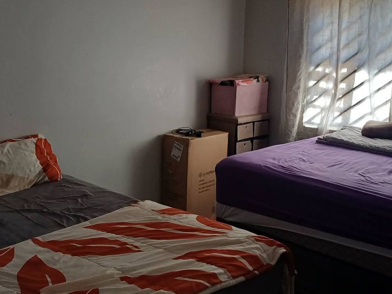A bedroom featuring natural light through a window with security bars, providing a functional space for rest.