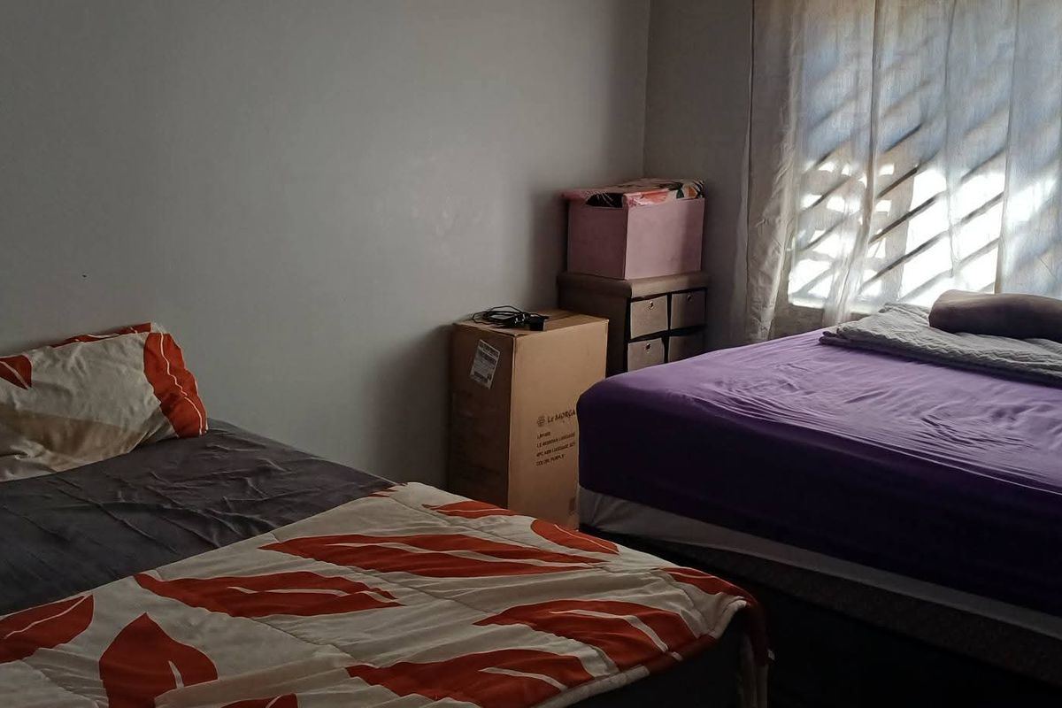 A bedroom featuring natural light through a window with security bars, providing a functional space for rest.