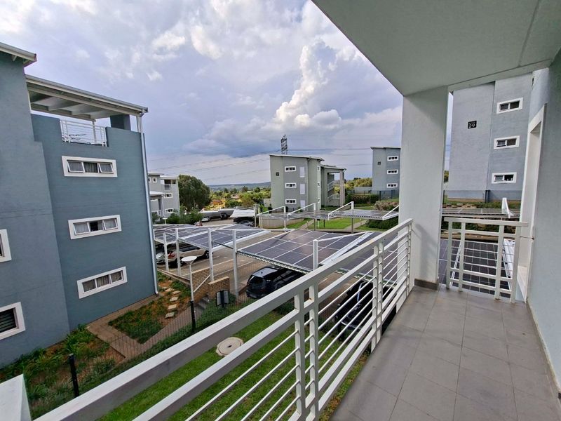 A spacious balcony with tiled flooring and a metal balustrade, overlooking the apartment complex grounds and solar-covered parking bays.
