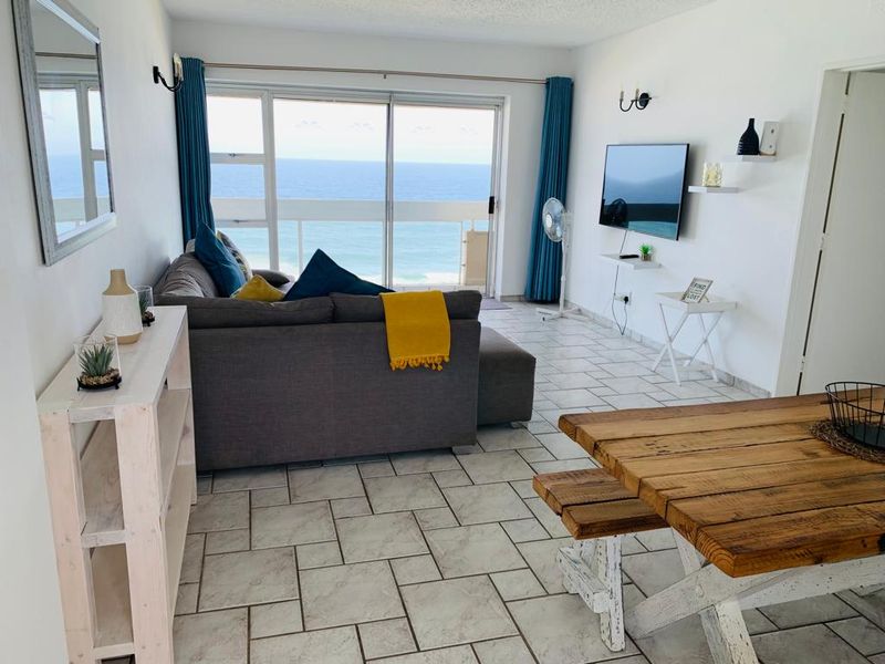Open-plan living and dining area featuring ceramic tile flooring and large sliding glass doors that provide direct access to a balcony with ocean views.