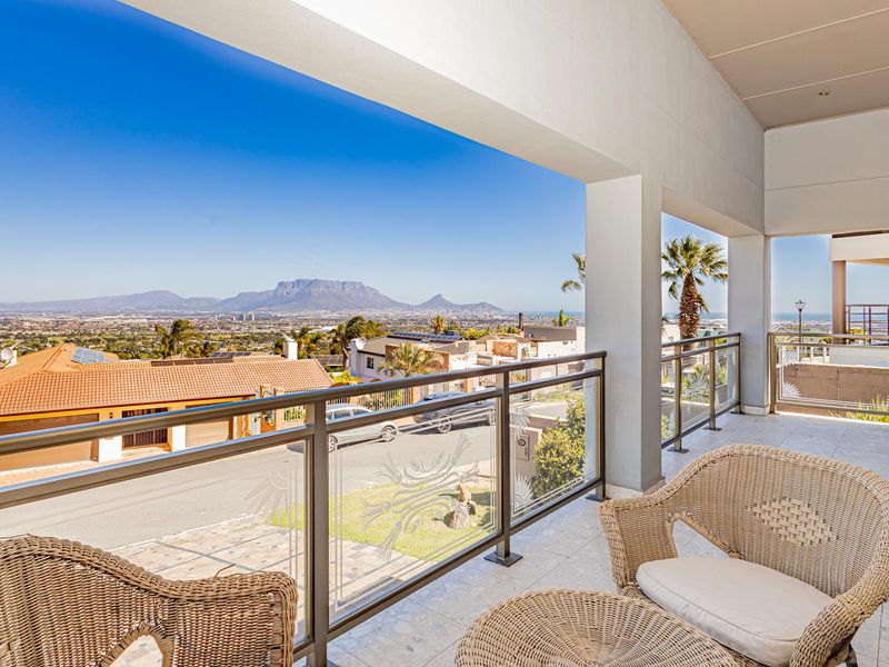 Spacious covered balcony featuring a modern glass balustrade and tiled flooring, offering expansive panoramic views of the surrounding landscape and mountains.