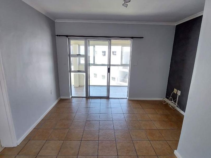 An empty living room featuring tiled flooring, neutral walls, and a sliding glass door providing access to an outdoor balcony area.