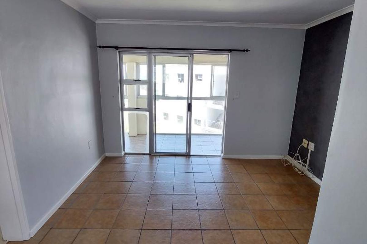 An empty living room featuring tiled flooring, neutral walls, and a sliding glass door providing access to an outdoor balcony area.