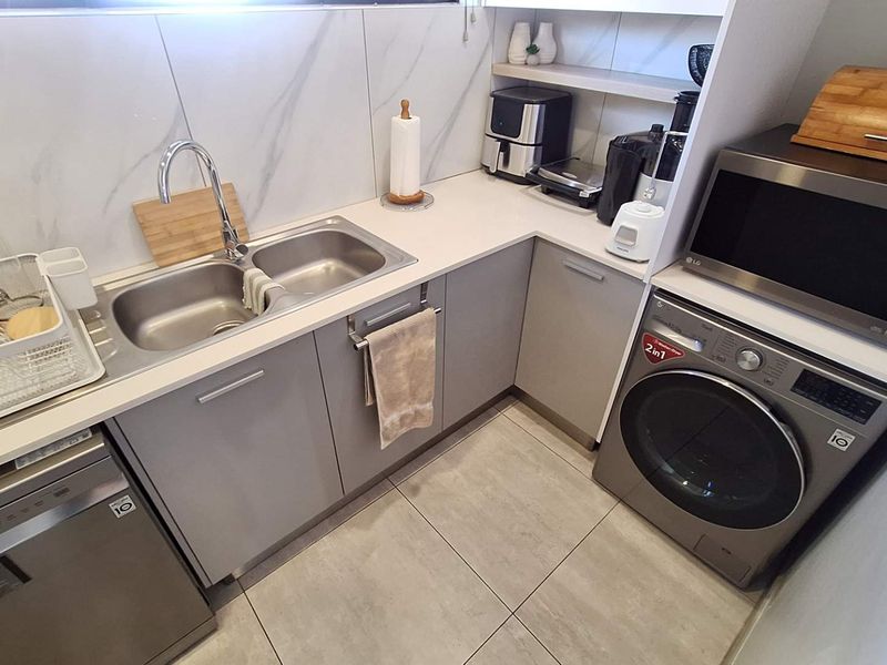 Modern scullery featuring sleek grey cabinetry, stone countertops, marble-look splashback, double sink, and integrated laundry and dishwasher appliances.