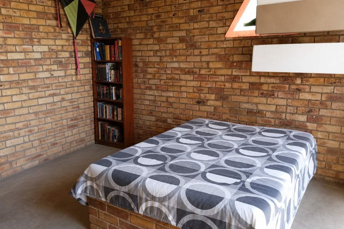 A rustic bedroom featuring exposed face-brick walls and a built-in brick bed base with polished concrete flooring.