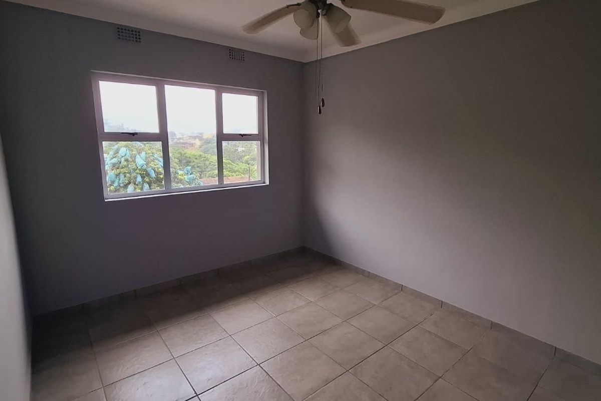 A clean, empty bedroom featuring neutral grey walls, tiled flooring, and a central ceiling fan with integrated lighting.