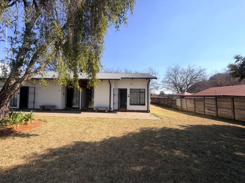 Rear view of the property featuring a paved patio area, corrugated metal roof, and a spacious garden enclosed by a precast concrete boundary wall.