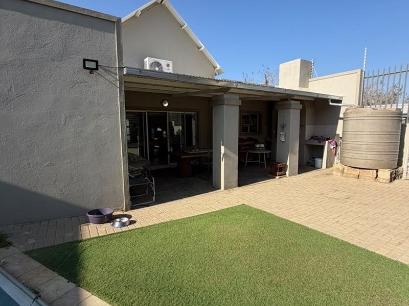 Rear exterior view featuring a covered patio, paved courtyard, artificial lawn, swimming pool, and a water storage tank.