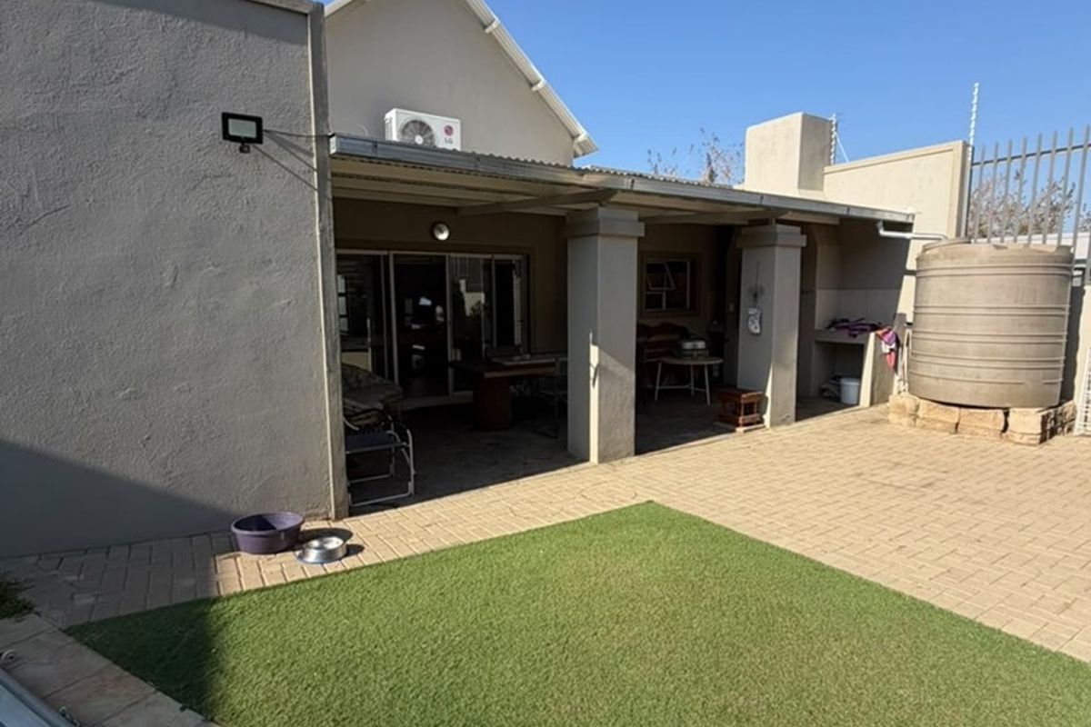 Rear exterior view featuring a covered patio, paved courtyard, artificial lawn, swimming pool, and a water storage tank.