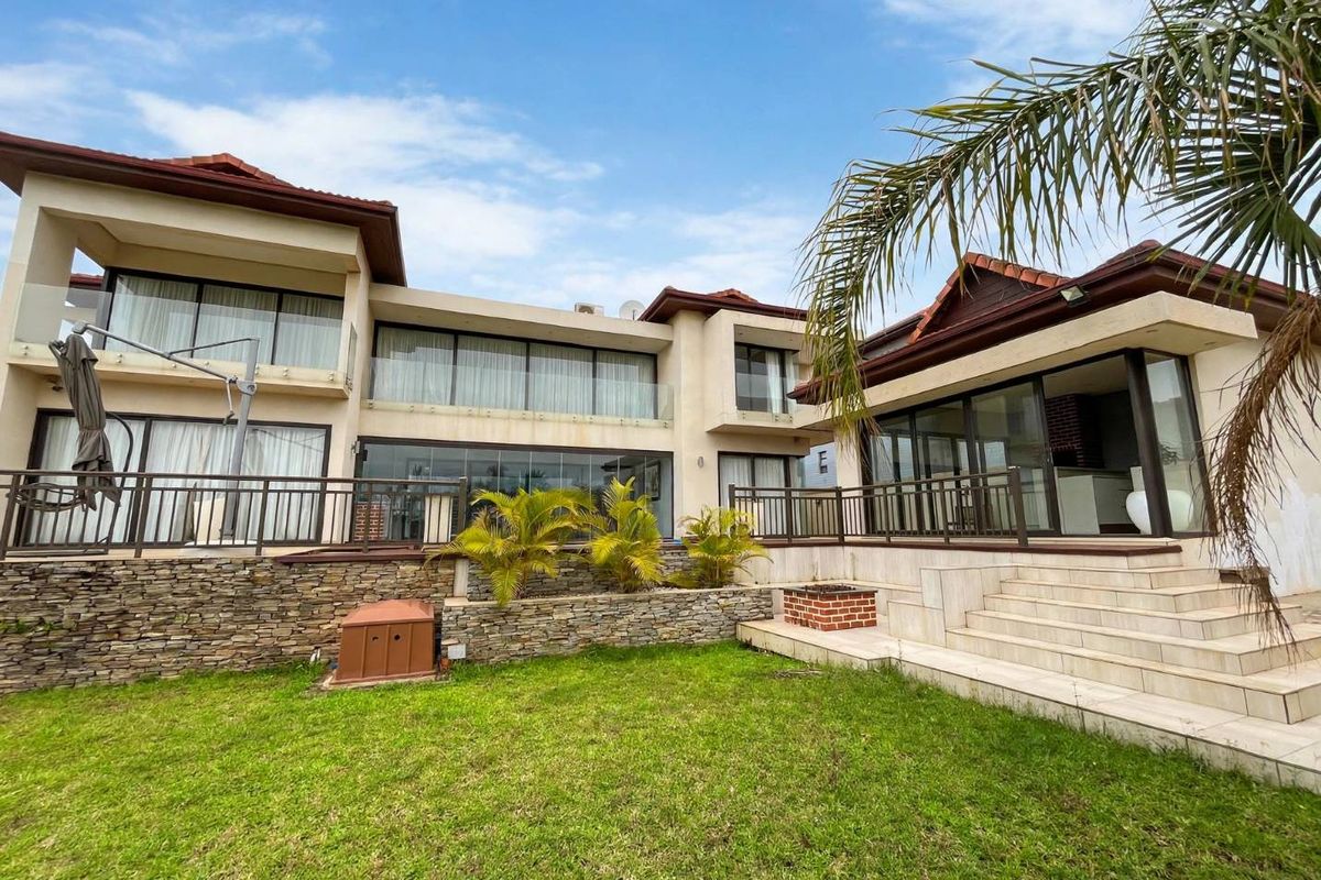 Rear view of a multi-level home featuring a spacious tiled patio, glass balustrades, stone retaining walls, and large sliding doors leading to the garden.