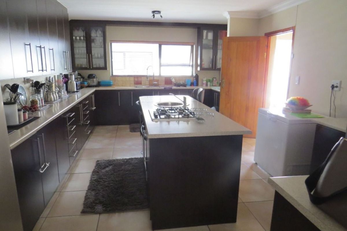 Spacious kitchen featuring dark cabinetry, a central island with a built-in gas hob, stone countertops, and tiled flooring.