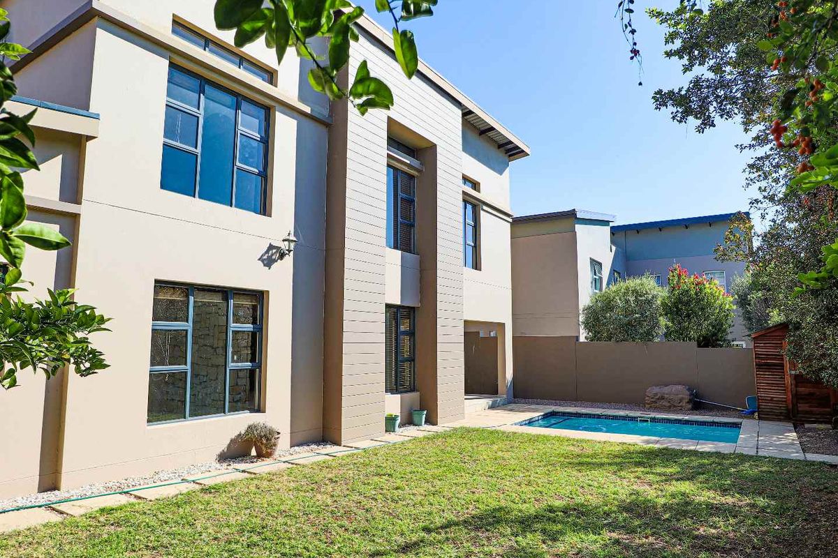 A well-maintained rear exterior view featuring a private swimming pool, landscaped lawn, and modern multi-story building facade with large windows.