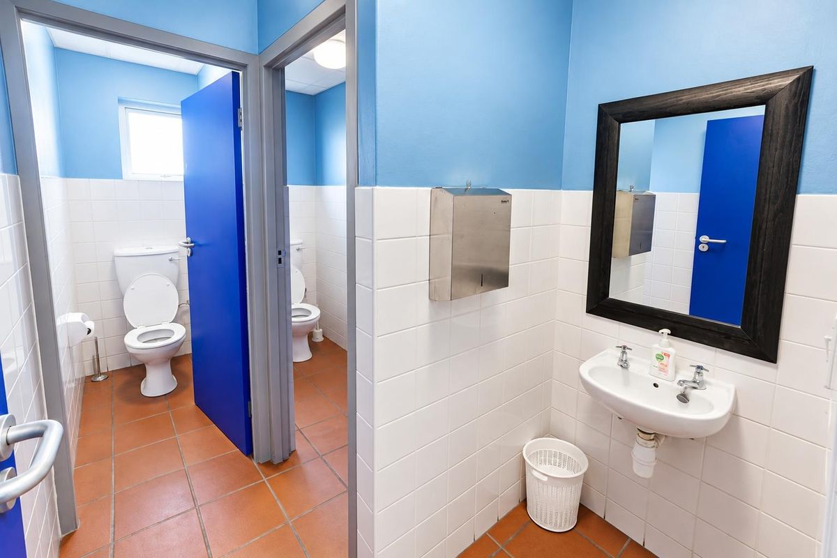 Functional office restroom facility featuring tiled walls and floors, dual-flush toilets, and a wall-mounted washbasin with a mirror.
