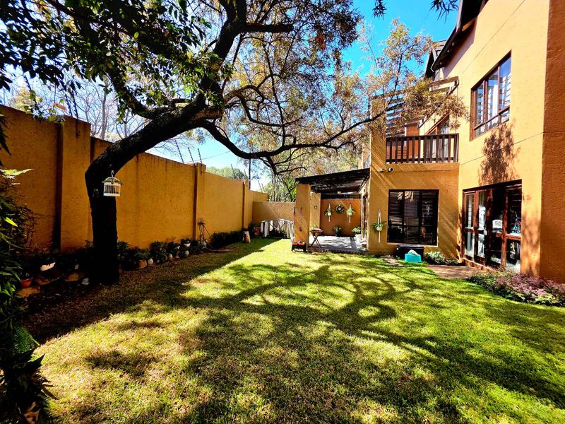 A private rear garden featuring a lawn, mature tree, perimeter wall, and a covered patio area attached to the apartment building.