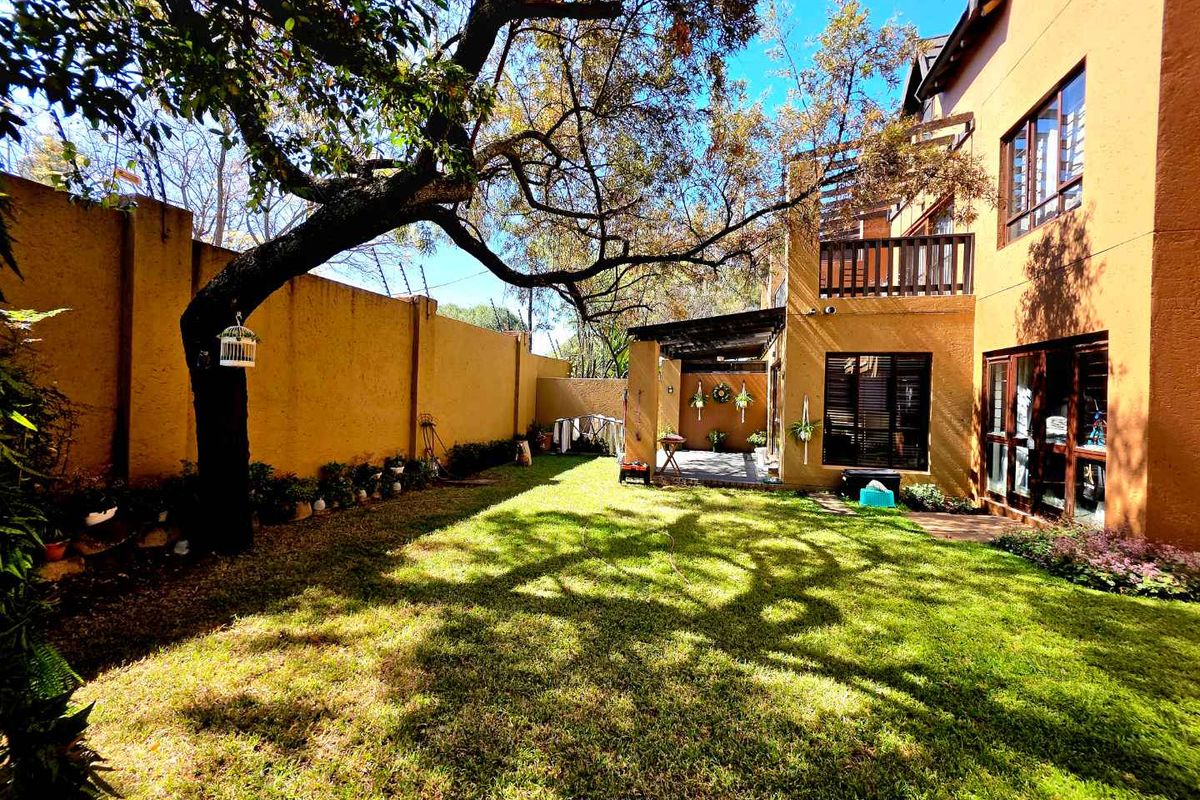 A private rear garden featuring a lawn, mature tree, perimeter wall, and a covered patio area attached to the apartment building.