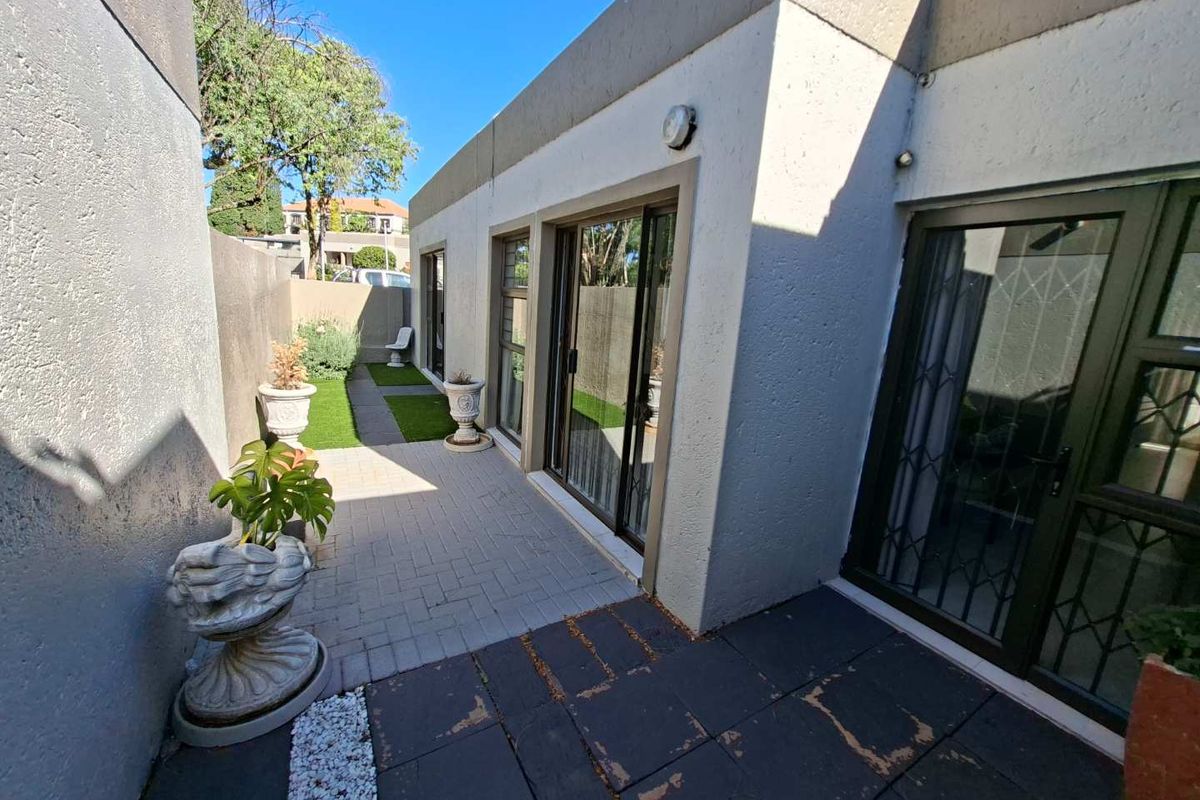 A rear exterior view of the townhouse featuring a paved patio area, sliding glass doors with security gates, and a small artificial grass garden.