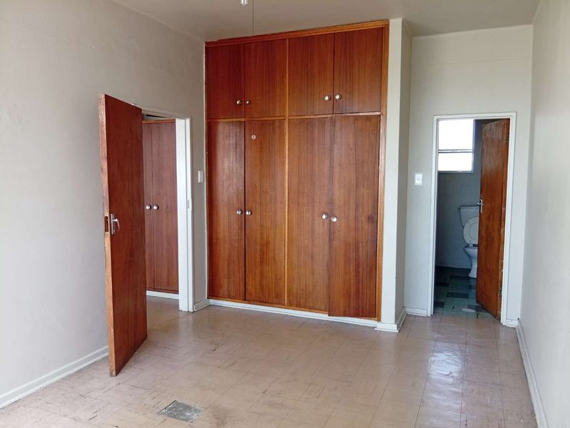 An empty bedroom featuring built-in wooden cupboards, tiled flooring, and direct access to an en-suite bathroom.