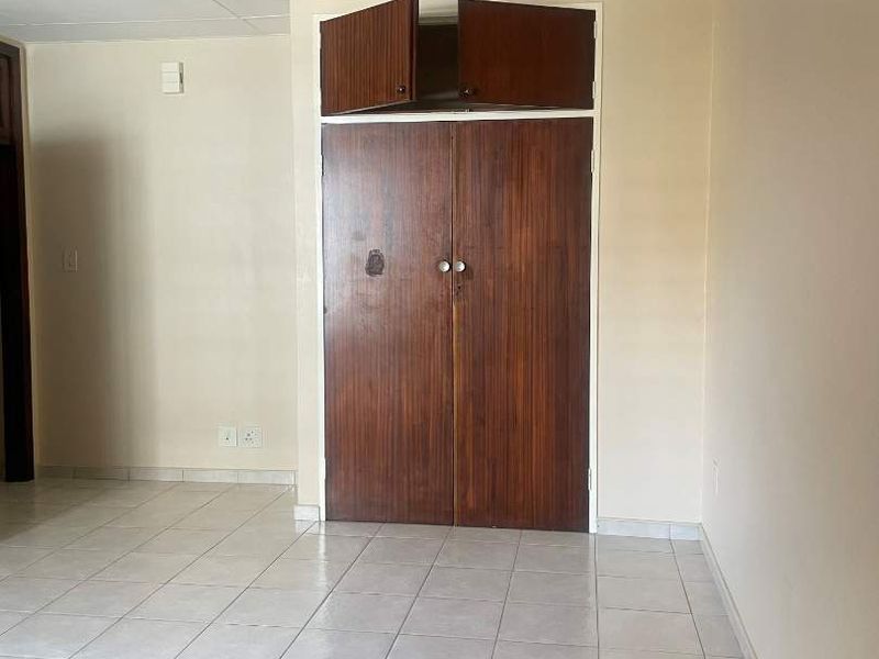 An empty bedroom featuring tiled flooring and a dated built-in wooden wardrobe with overhead storage compartments.