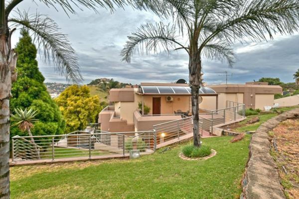 Rear view of the property featuring a multi-level terrace with metal railings, landscaped garden, and elevated views of the surrounding area.