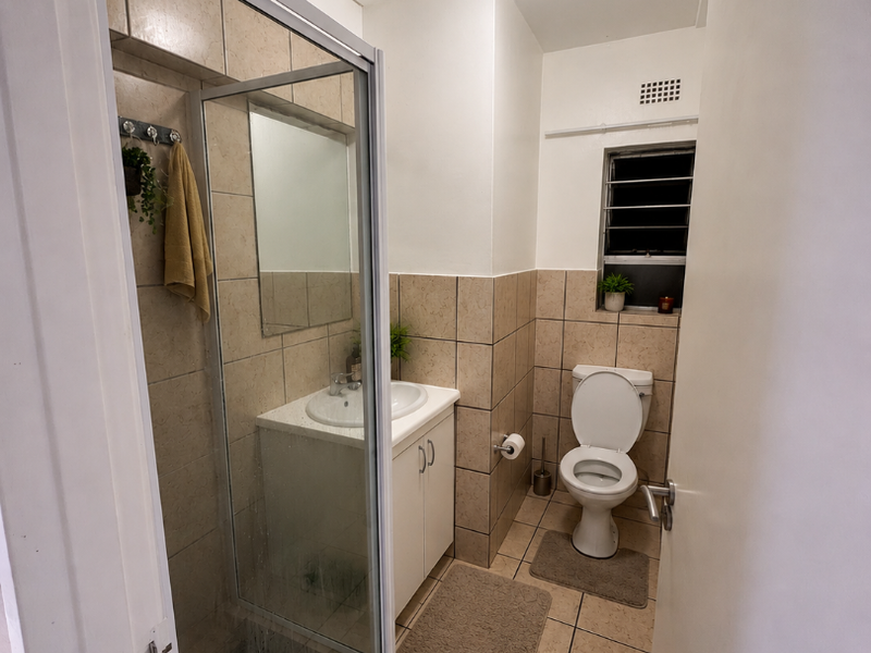 A functional bathroom featuring a shower enclosure, vanity with integrated basin, and toilet, finished with neutral wall and floor tiling.