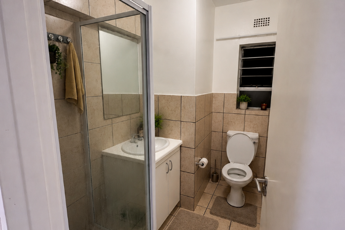 A functional bathroom featuring a shower enclosure, vanity with integrated basin, and toilet, finished with neutral wall and floor tiling.