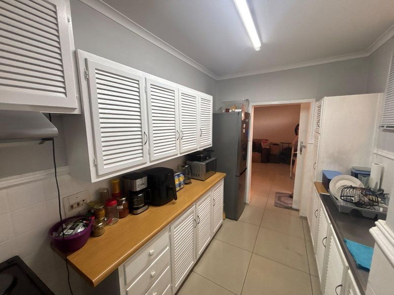 A functional kitchen featuring white louvered cabinetry, laminate countertops, and tiled flooring, providing a practical workspace with direct access to the adjacent living area.